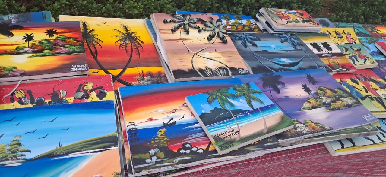 Vibrant hand-painted Jamaican landscape canvases at an outdoor market