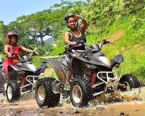 Riders on ATVs splashing through a muddy jungle trail