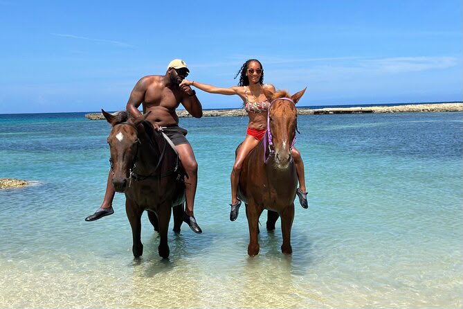 Couple horseback riding through shallow turquoise sea water